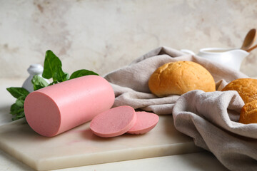 Board with slices of tasty boiled sausage, bread and basil on grunge grey background