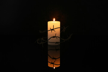 Burning candle with barbed wire on dark background. Day of Remembrance