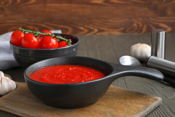 Frying pan of tomato sauce and garlic on wooden background