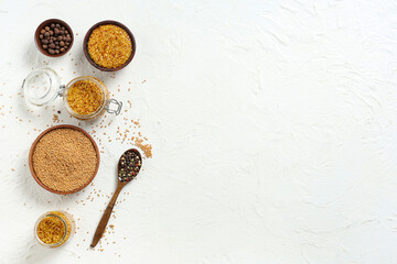 Jars and bowls of Dijon mustard with seeds and peppercorn on white background