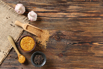 Bowl and spoon of Dijon mustard with peppercorn and garlic on wooden background