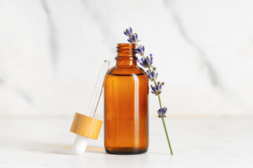 Bottle of lavender essential oil and  flowers on marble background, closeup