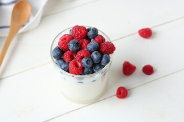Glass of tasty yogurt with fresh blueberries and raspberries on white wooden background
