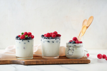 Glasses and jar of tasty yogurt with fresh blueberries and raspberries on white background