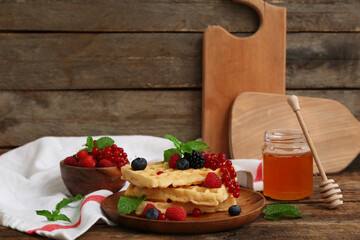 Plate of sweet Belgian waffles with different fresh berries and jar of honey on wooden background