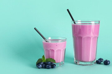 Glasses of fresh blueberry smoothie with mint and berries on turquoise background