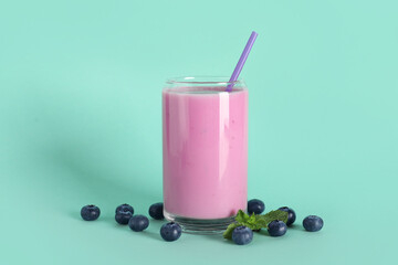 Glass of fresh blueberry smoothie with mint and berries on turquoise background