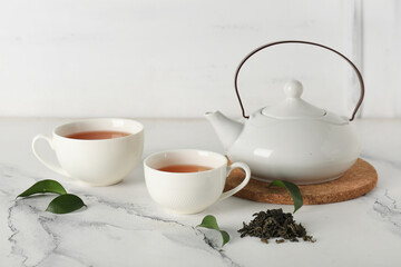 Cups and teapot of hot tea with dried leaves on white background