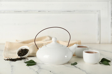 Bowls and teapot of hot tea with dried leaves on white background
