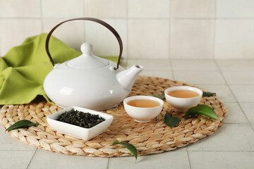 Bowls and teapot of hot tea with dried leaves on white tile background