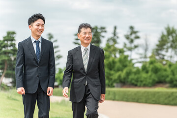 公園を歩く若いビジネスマンとシニア世代の男性ビジネスマン
