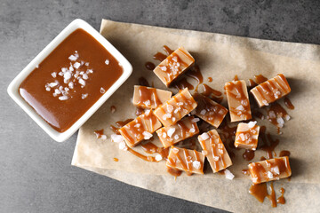 Tasty candies, caramel sauce and salt on grey table, top view