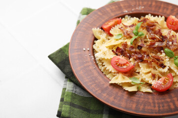 Tasty pasta with bacon, tomatoes and basil on white tiled table, space for text