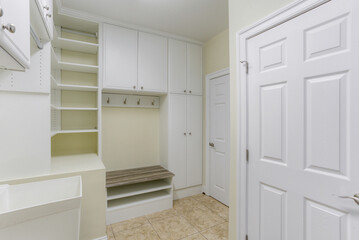 Organized Mudroom With White Built-In Cabinets, Bench, And Hooks On Tiled Floor