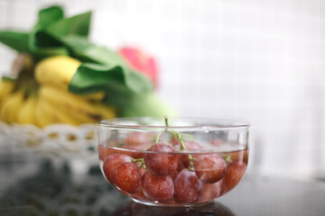 Selective Focus Grapes On Bowl With Water Againt Blurred Fruits And Vegetable Background. Healthy Food Concept