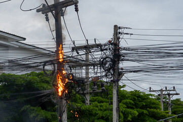 Electric pole engulfed in flames with tangled wires, posing a severe hazard in an urban residential...