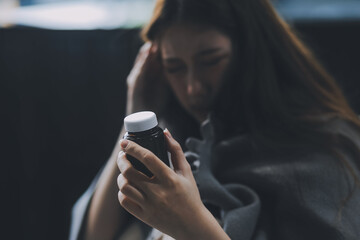 Fototapeta premium A woman with a cold with pills is treated at home chooses which drugs to take and self-medicates, checks the expiration date while sitting on the couch at home
