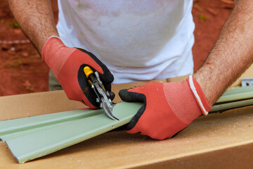 Worker cuts plastic vinyl siding to size with of scissors before installing it