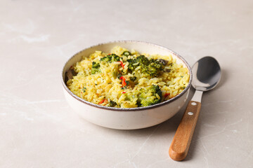Pilaf in bowl and spoon on light background, close up