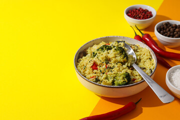 Pilaf in bowl, spoon and spices on yellow background, space for text
