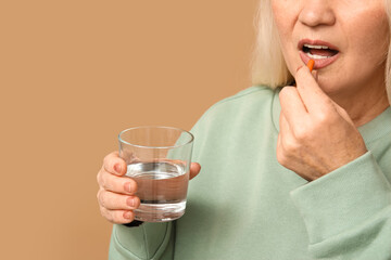 Beautiful mature woman with pill and glass of water on brown background