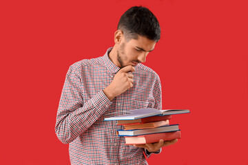 Thoughtful young man reading books on red background