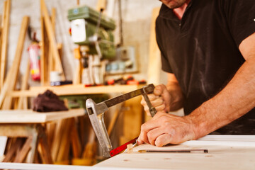 Carpenter using a hacksaw to cut wood in workshop