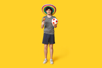 Young male football player with sombrero, soccer ball and maracas on yellow background