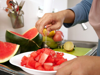 Asian muslim woman cutting slicing watermelon fruits in kitchen