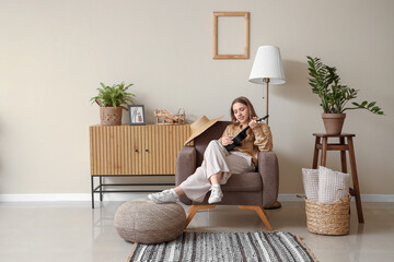 Beautiful young woman playing ukulele while sitting in armchair in living room