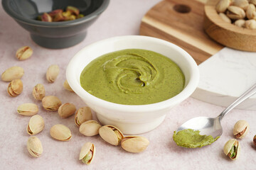 Bowl with tasty pistachio paste and spoon on pink grunge background