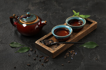 Teapot with cups, spoon of dry tea and leaves on black grunge background