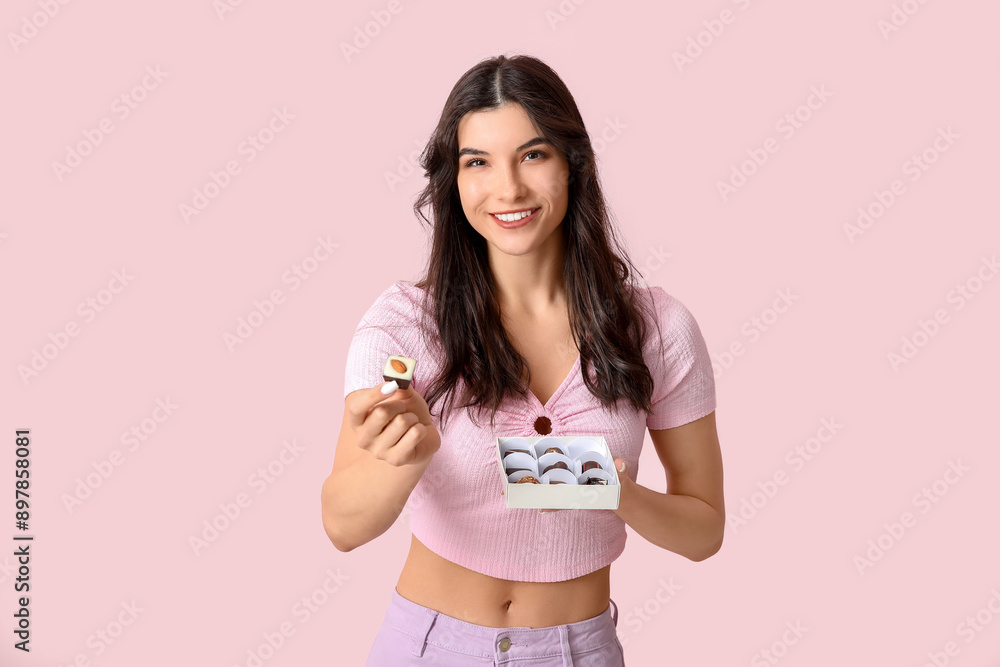 Poster Happy young woman with box of delicious chocolate candies on pink background