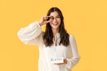 Young woman with box of delicious chocolate candies on yellow background