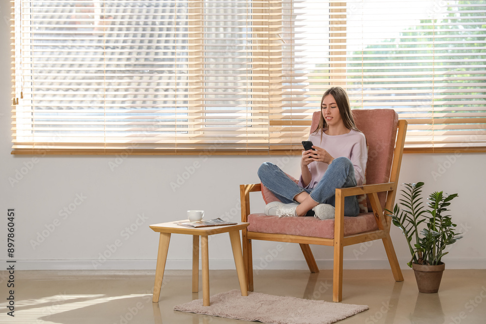 Canvas Prints young woman using mobile phone while sitting in armchair with cushion in room