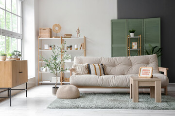 Soft sofa with cushions, coffee table with picture and decorative olive tree in living room