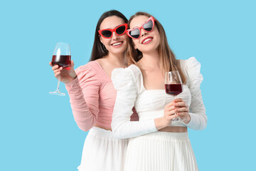 Beautiful young lesbian couple with glasses of wine on blue background