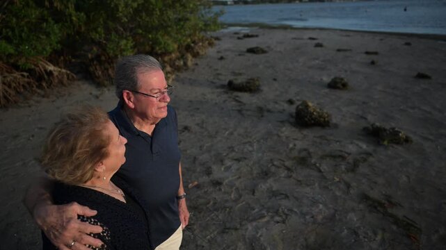 senior citizen couple with his arm around wife watch the sunset on a beach in Florida