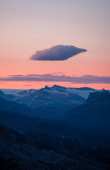Midnight sun in arctic summer landscape of Norway. Silhouettes of mountain ranges in sunset colours of blue, orange and purple. Few clouds on clear dawn and dusk sky. Moody mountain range landscape