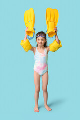 Cute little girl in swimsuit with inflatable armbands and flippers on blue background