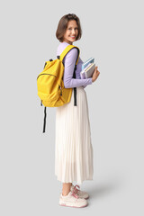 Beautiful female student with backpack and books on grey background