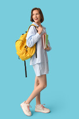 Beautiful female student with backpack and notebooks on blue background