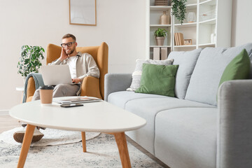 Young bearded man in eyeglasses using laptop at home