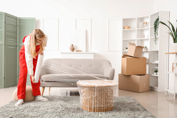 Female worker wrapping coffee table with stretch film in room