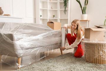 Female worker wrapping sofa with stretch film in room