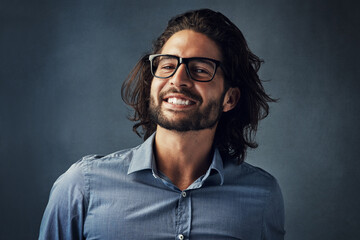 Fototapeta premium Smile, glasses, and portrait of man in studio with confidence, casual fashion and creative business style. Face, pride and happy businessman with professional design consultant on blue background
