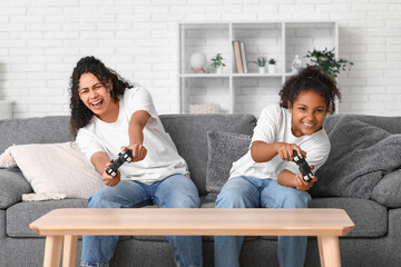 Beautiful young happy African-American mother with her daughter playing video games at home
