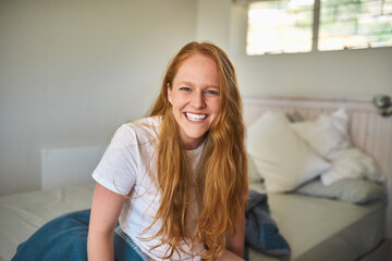 Obraz premium Portrait, home and happy woman in bedroom to wake up after resting for peace and calm in apartment. Face, morning and smile of girl on mattress for comfort, relax and ready to start day in Ireland