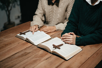 Group of Christians sit together and pray around a wooden table with blurred open Bible pages in their homeroom.