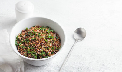 White bowl with boiled buckwheat and kale on a gray background, top view. Healthy homemade vegan food